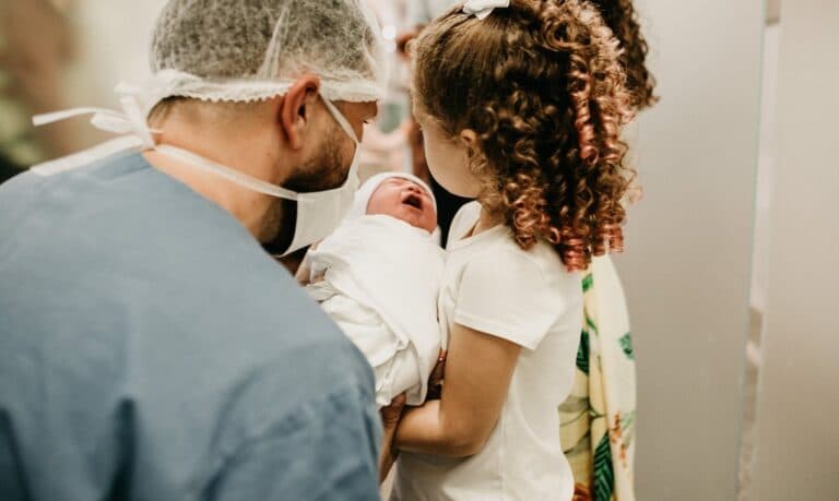 Lekarz wraz z dziewczynką trzymają płaczącego noworodka